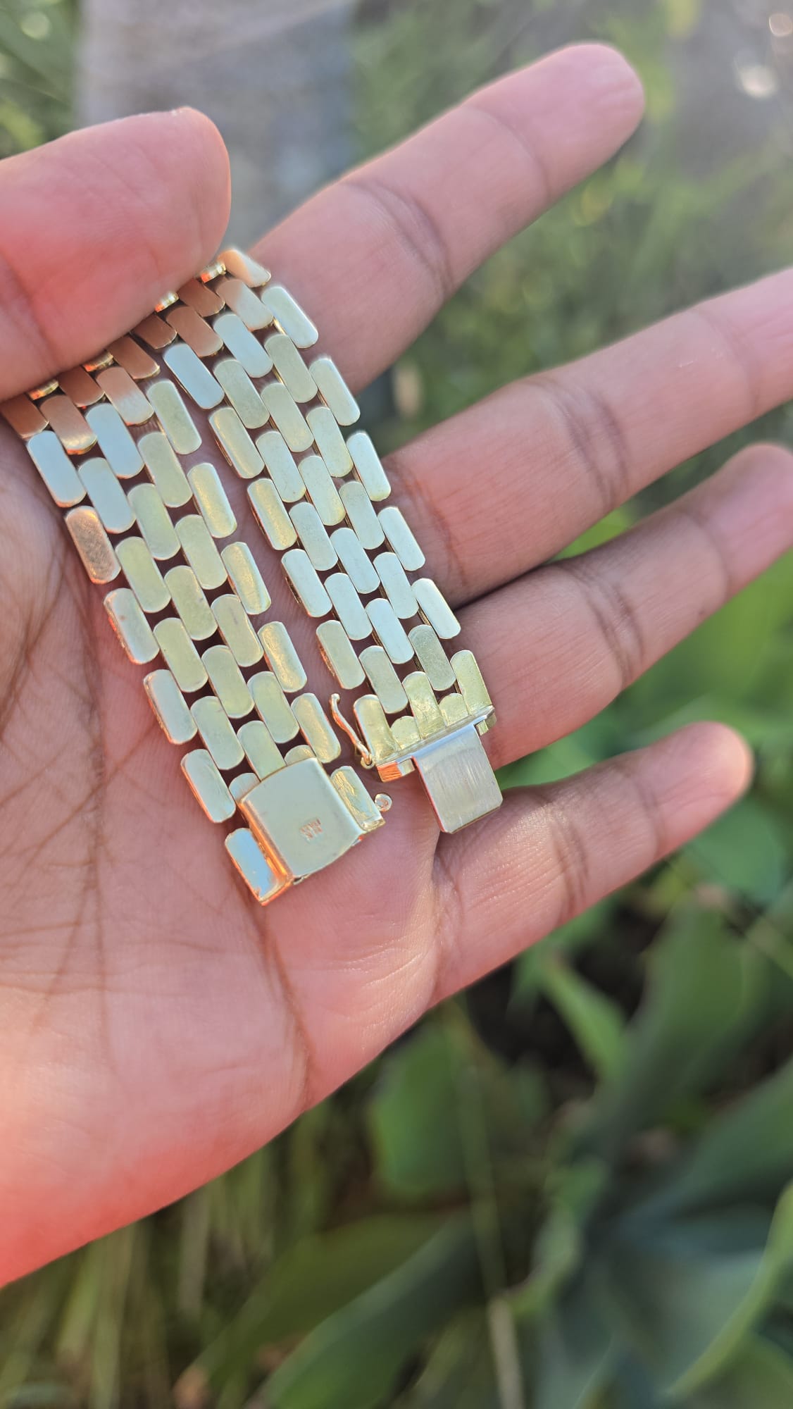 Gold chain links held between fingers with a blurred natural background