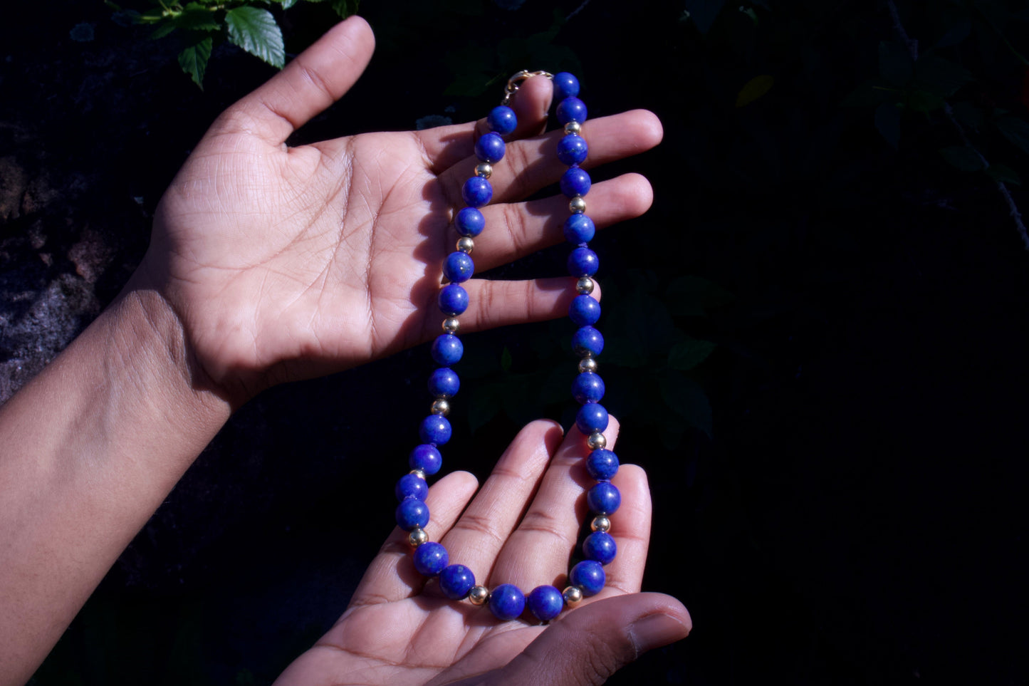 Hand holding a blue beaded necklace against a dark background