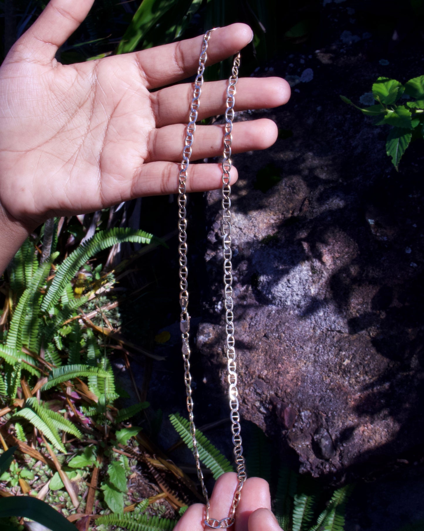 Hand holding a chain with a natural background of rocks and plants