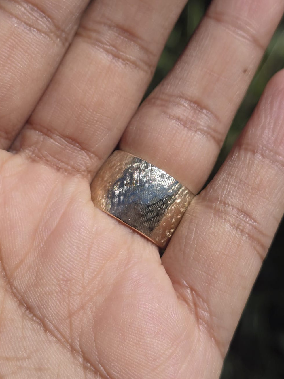 Hand wearing a textured silver ring with a blurred natural background