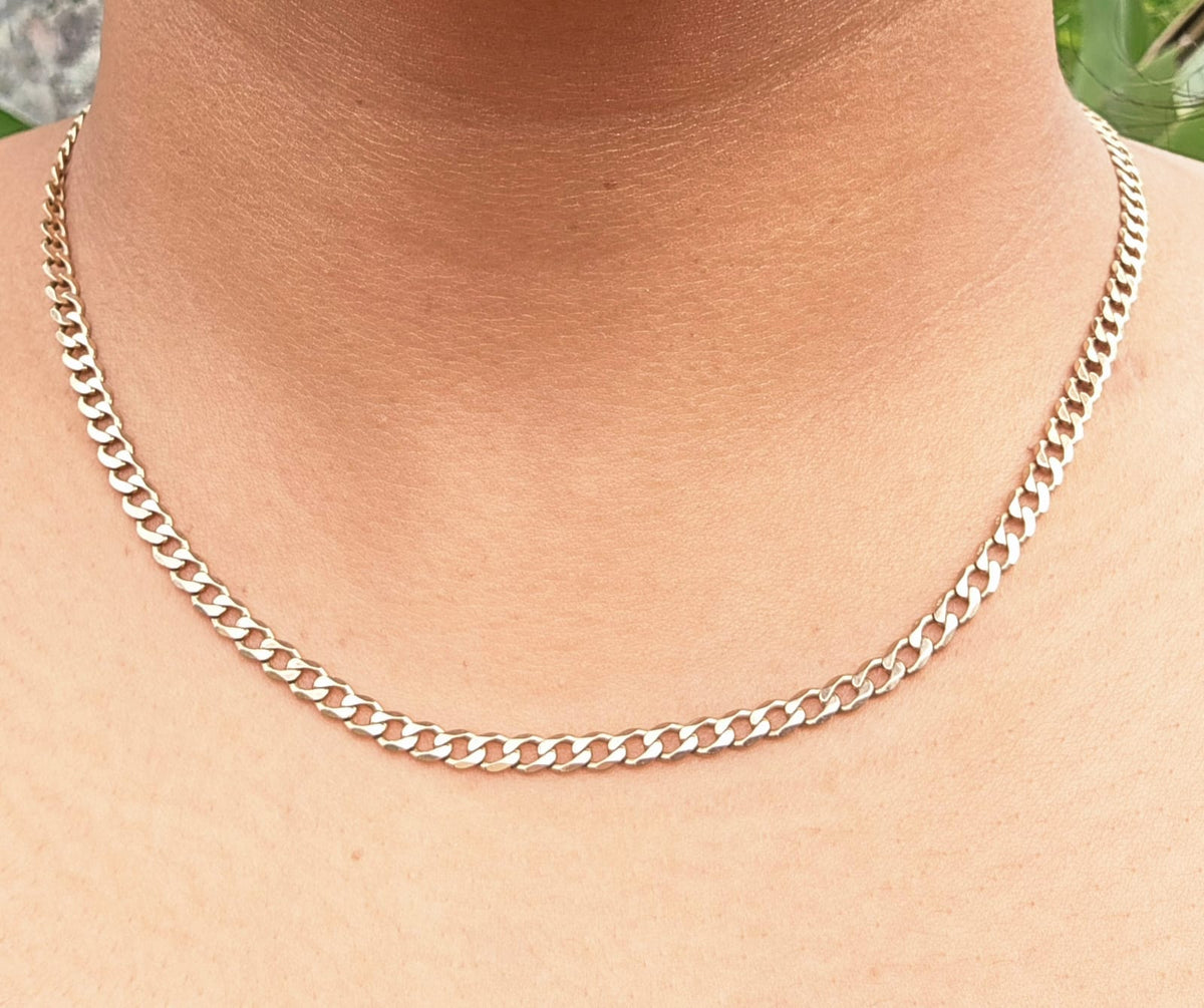 A close-up of a silver Cuban link chain necklace worn on a person's neck and upper chest.