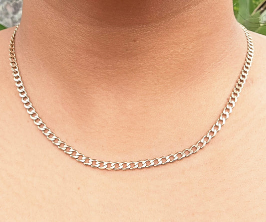 A close-up of a silver Cuban link chain necklace worn on a person's neck and upper chest.