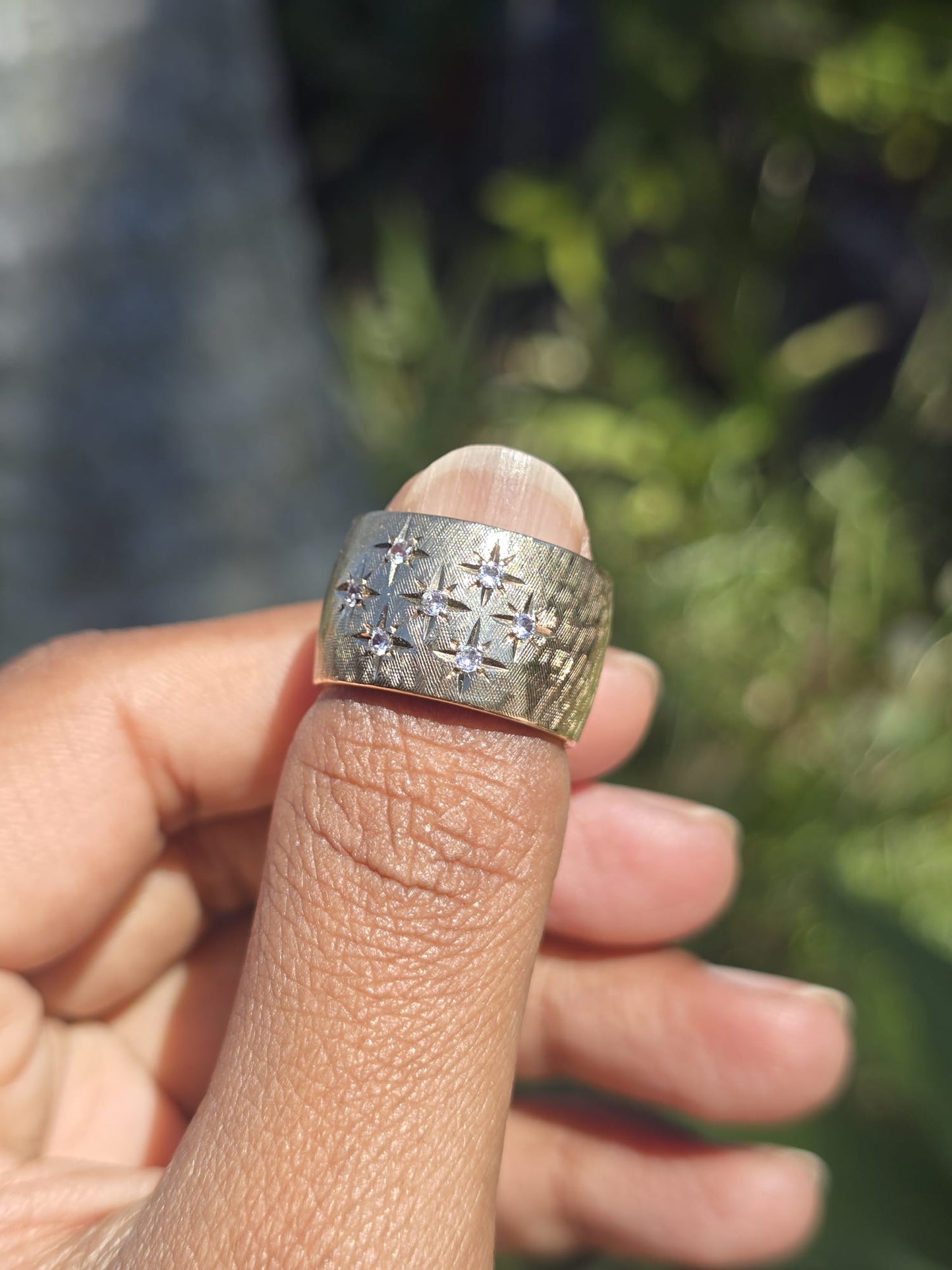Gold ring with diamonds on a finger against a blurred natural background