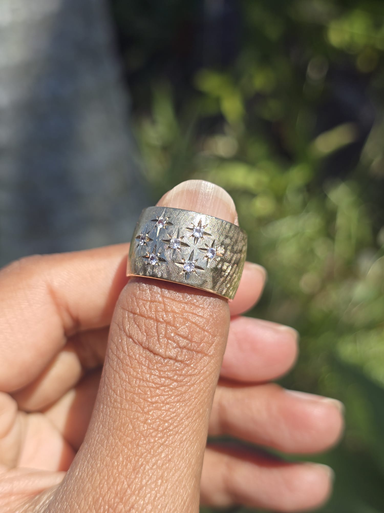 Gold ring with diamonds on a finger against a blurred natural background