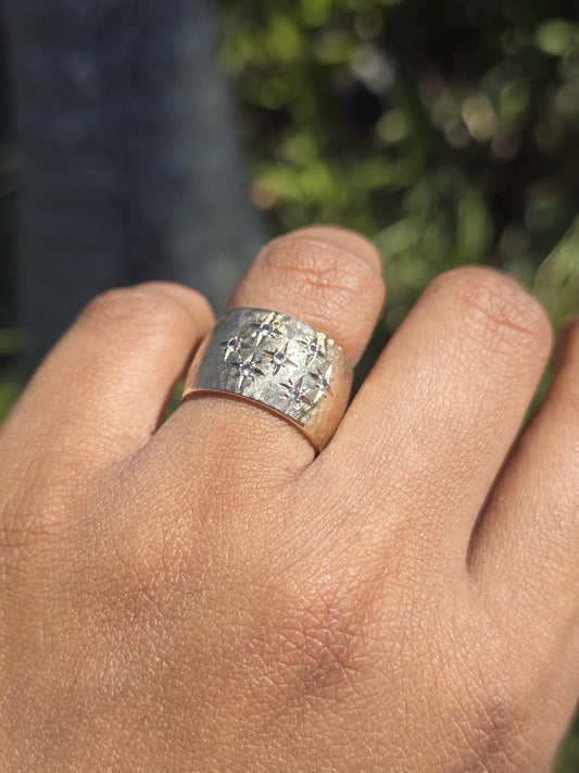 Hand wearing a gold textured ring with a blurred natural background