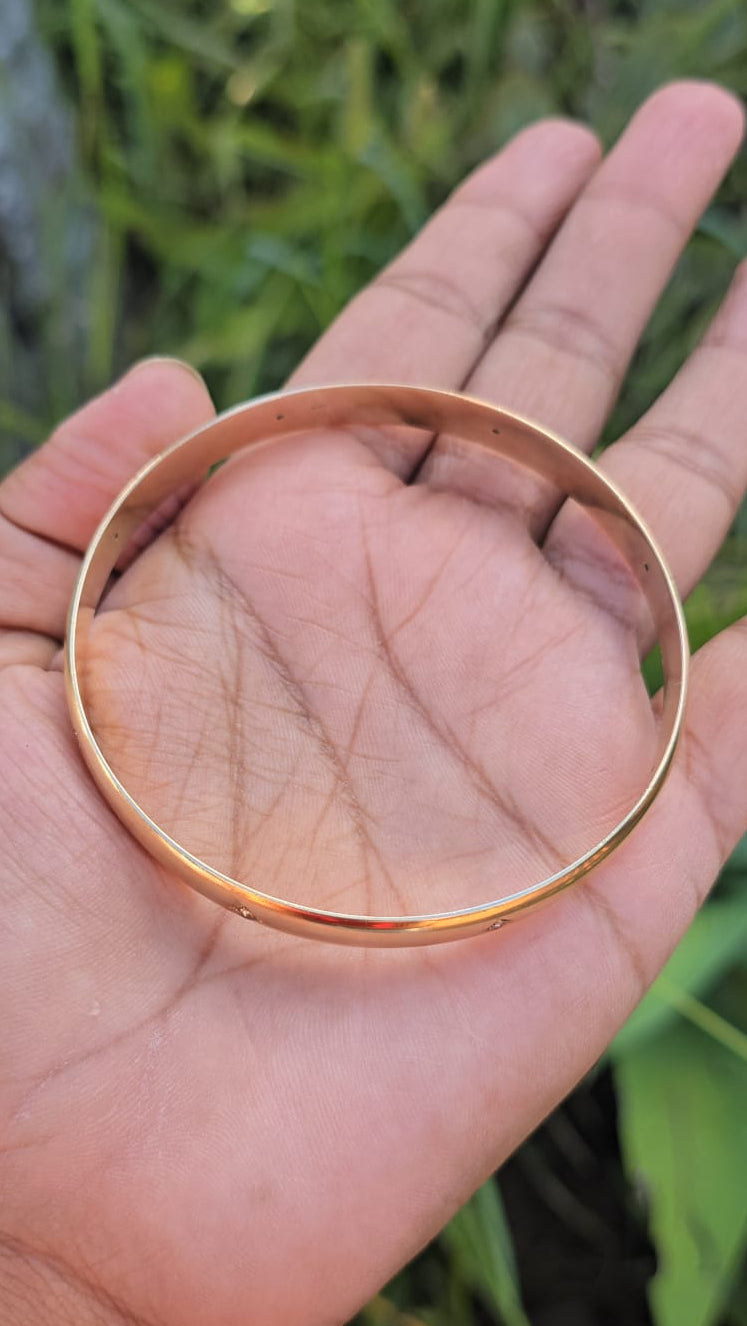 Hand holding a gold bracelet with a natural background