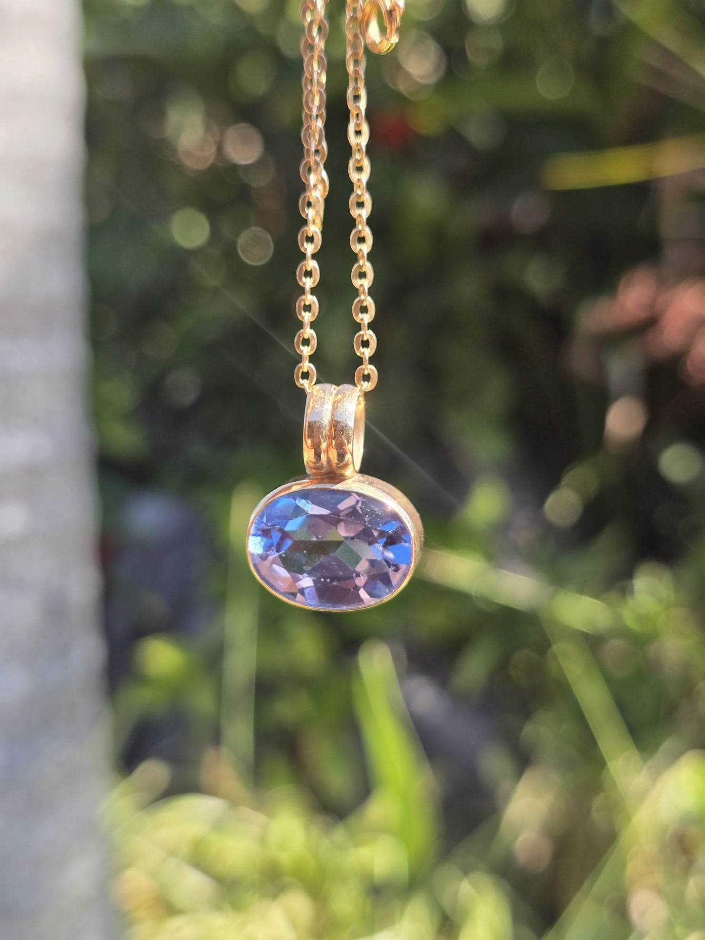 Gold necklace with a blue gemstone pendant against a blurred green background