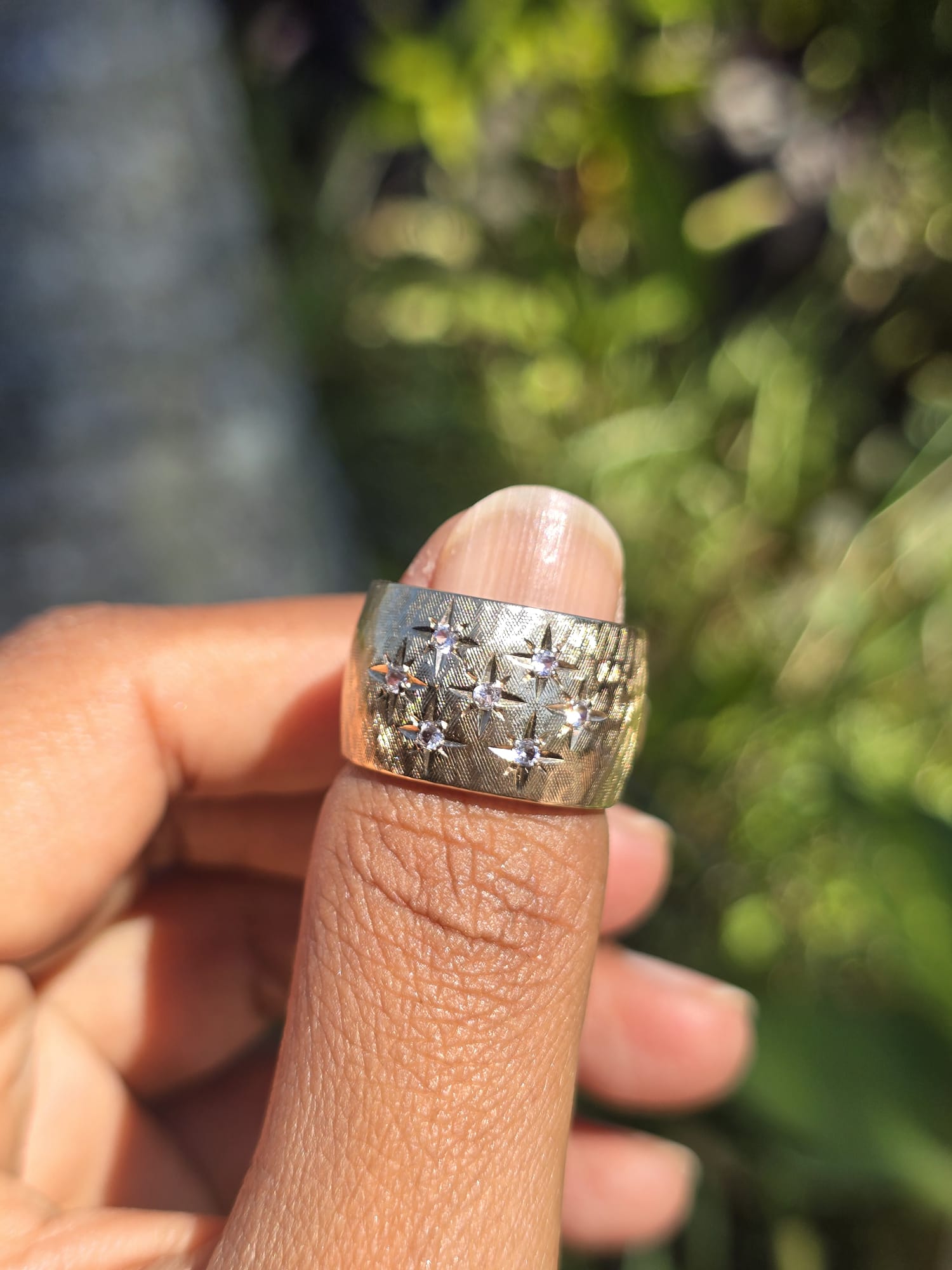 Gold ring with diamonds on a finger against a blurred natural background