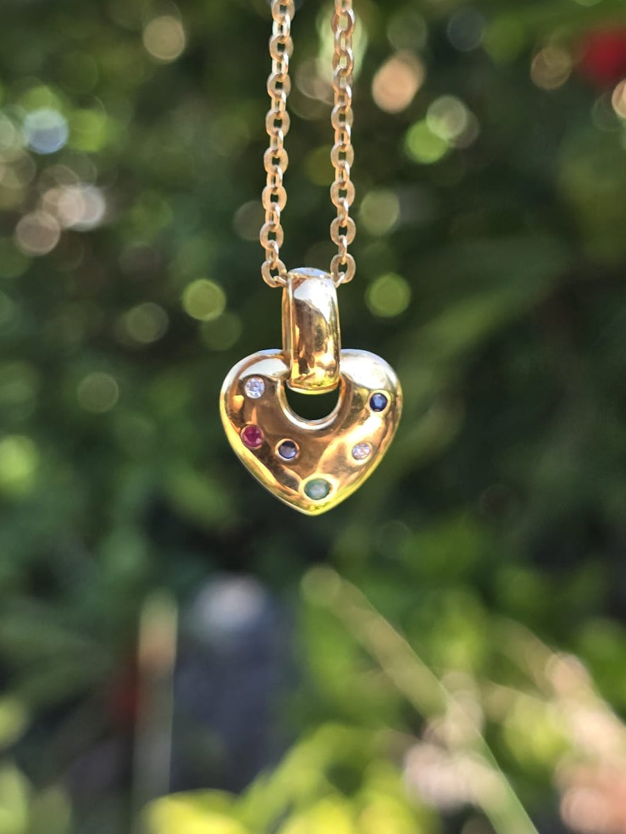Gold heart-shaped necklace with colorful stones against a blurred green background