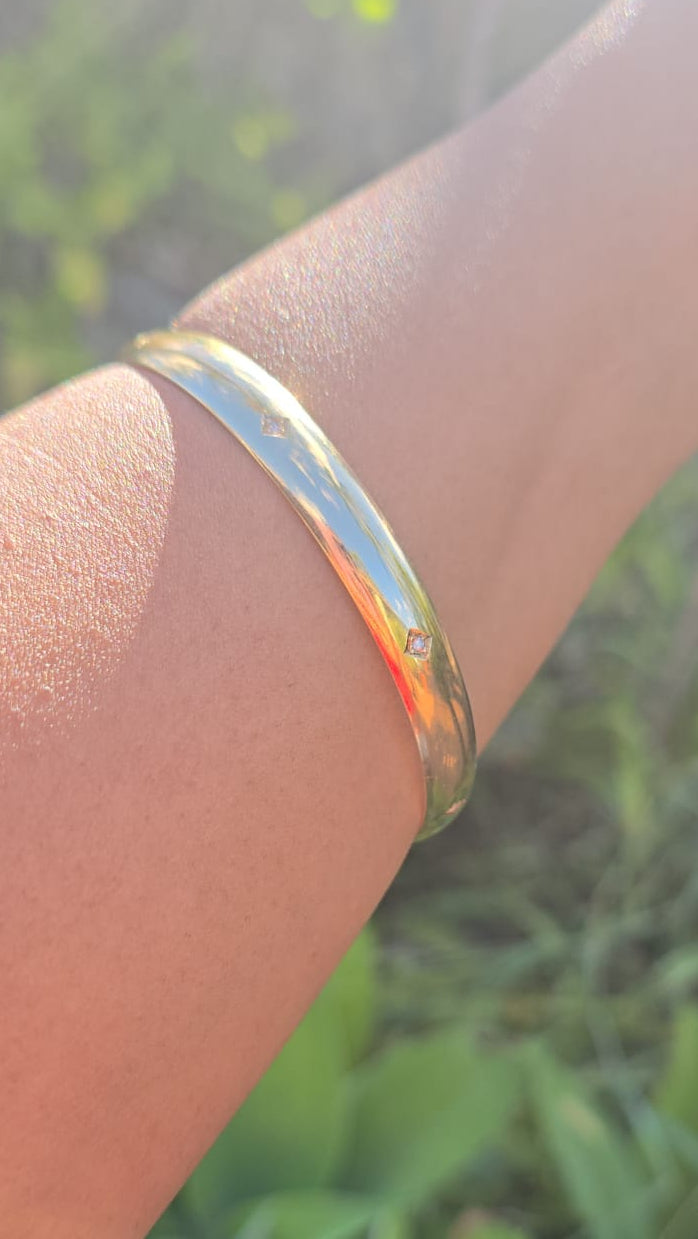 Gold bracelet on a wrist with a blurred green background