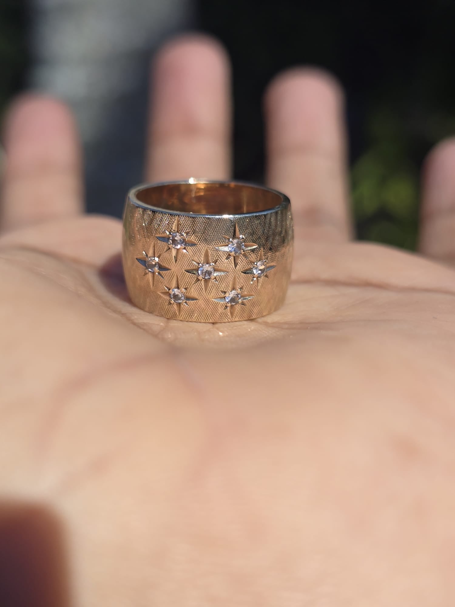 Gold ring with star designs on a hand against a blurred background