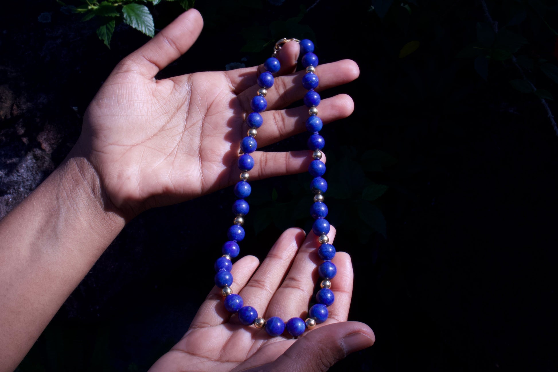 Hand holding a blue beaded necklace against a dark background