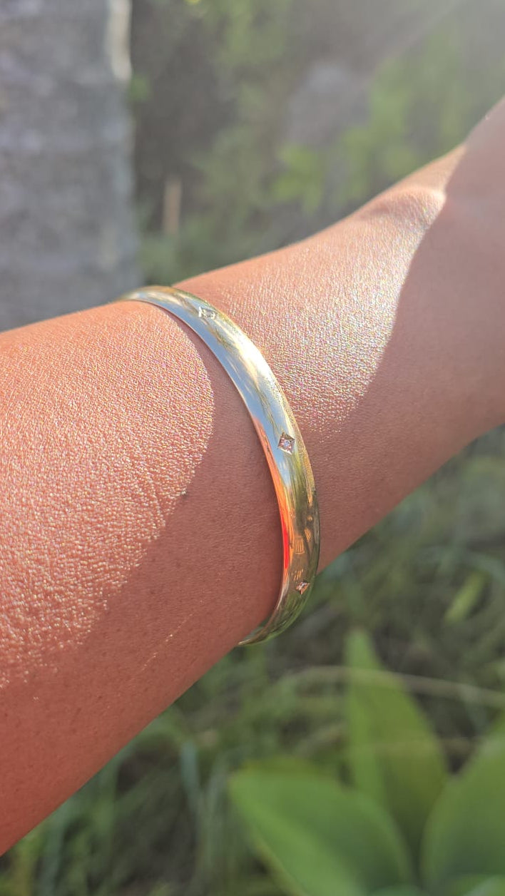 Gold bracelet on a wrist with a blurred natural background
