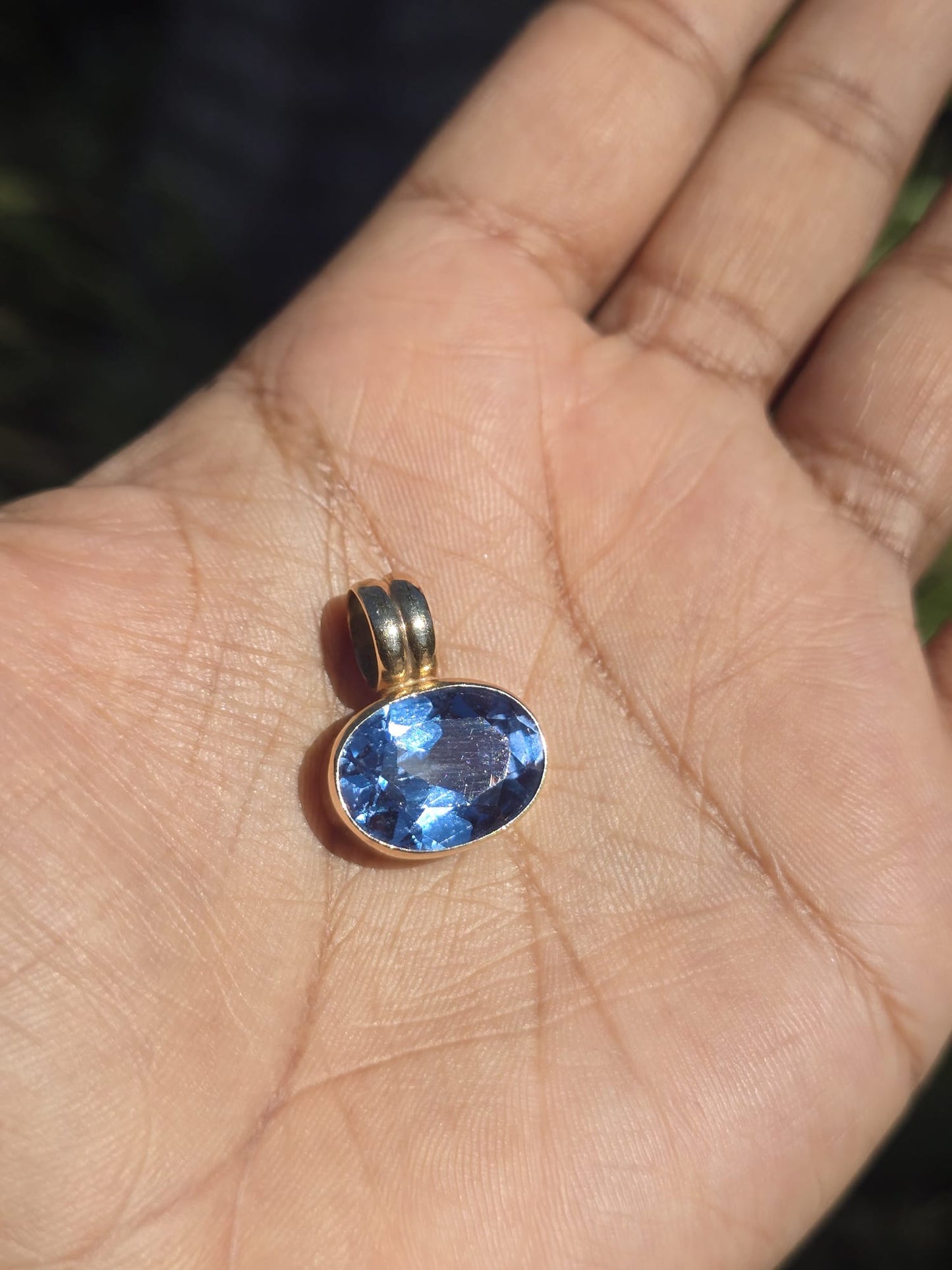 Gold pendant with a blue gemstone held in a hand