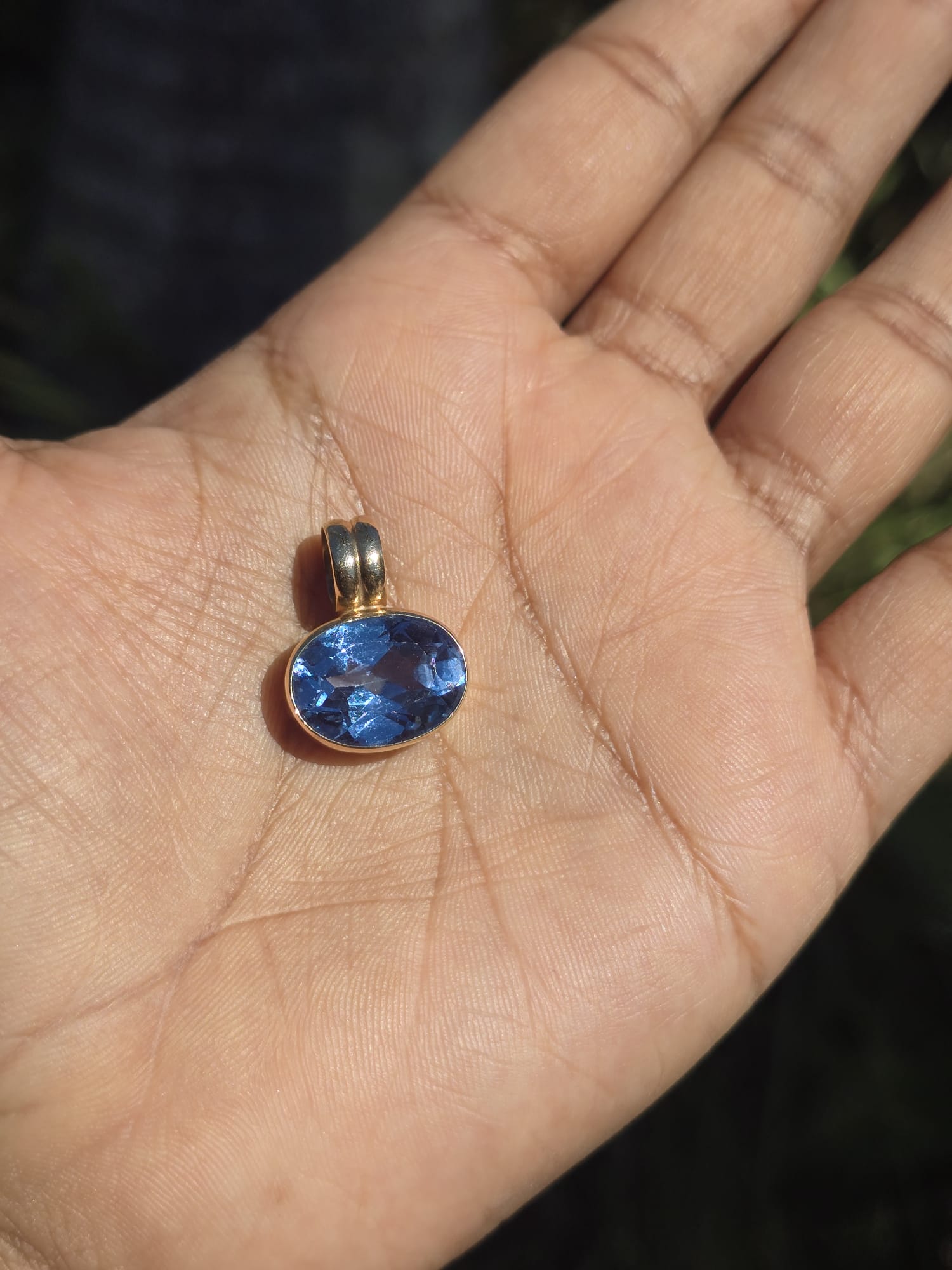 Blue gemstone pendant on a gold chain held in a hand